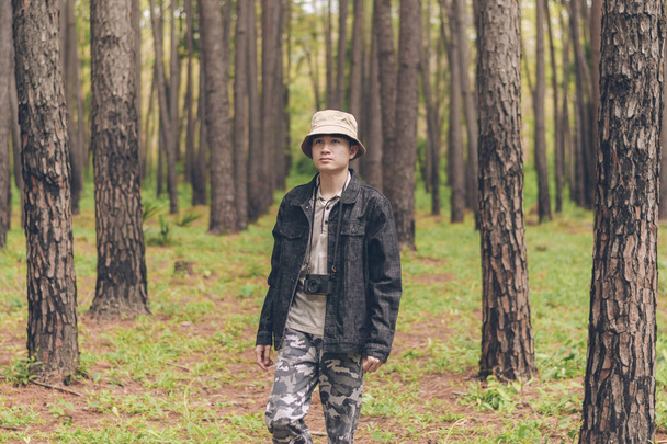 Asia man wears shirt and denim jacket, hat, and camouflage pants are walking and taking photos at the forest. - Foto, Imagen