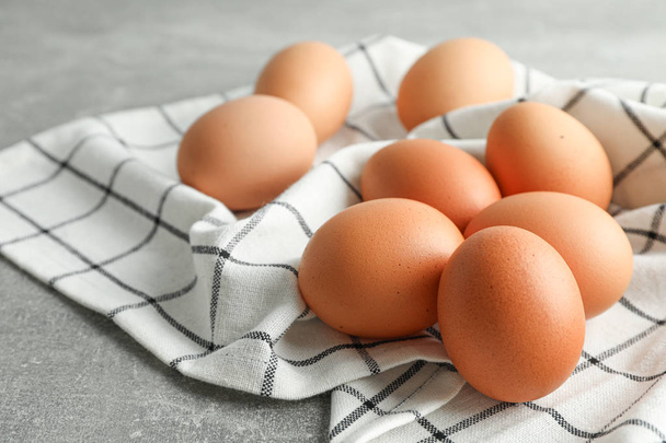 Коричневые куриные яйца в кухонном полотенце на сером фоне, пространство fo
 - Фото, изображение