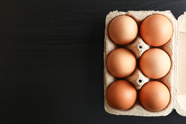 Brown chicken eggs in carton box on black background, space for  - Фото, зображення