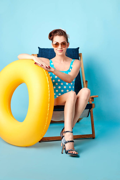loira em um maiô e óculos sentados em uma cadeira de praia com um círculo inflável
 - Foto, Imagem