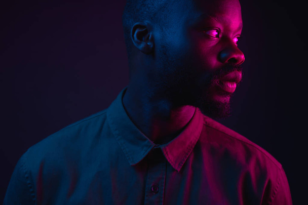 Dark neon portrait of young man with beard, wearer in shirt. Pink and blue light. Technology - 写真・画像