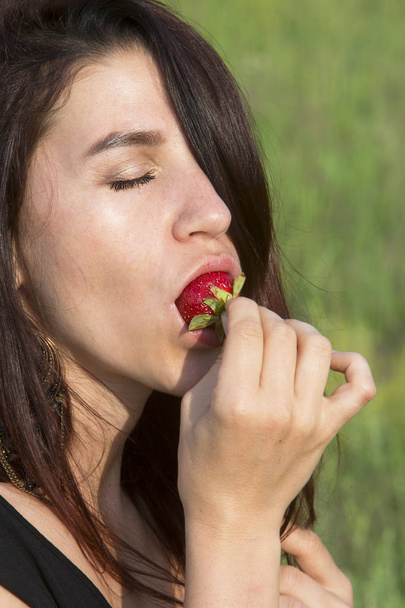 young beautiful woman gently eats ripe fresh strawberries - Foto, afbeelding