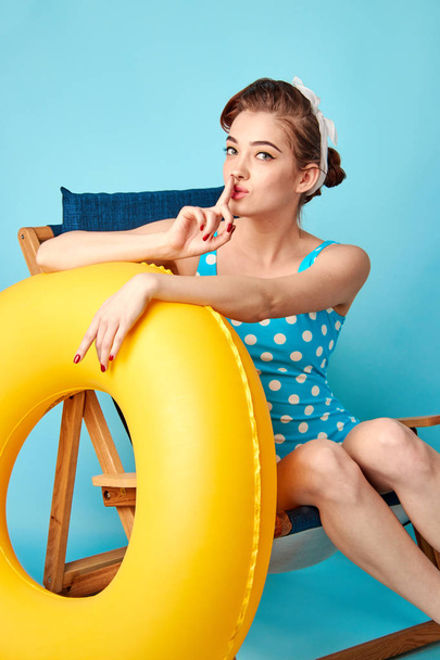 blondi uimapuvussa istuu kansituolilla puhallettavan ympyrän kanssa
 - Valokuva, kuva