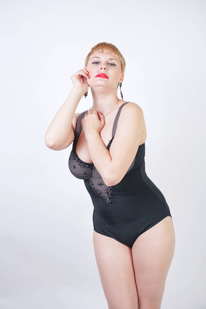 pretty short hair blonde woman with plus size body wearing retro black lingerie and posing on white studio background alone - Photo, Image