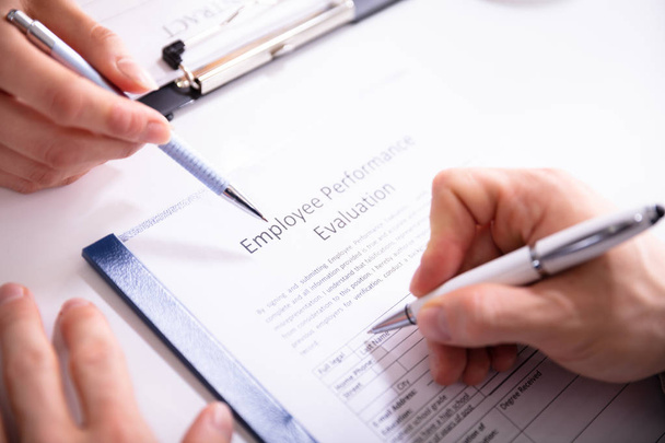 Primer plano de una persona que llena el formulario de evaluación del desempeño del empleado sobre el escritorio
 - Foto, imagen
