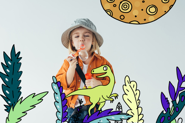 lindo niño en sombrero y camisa naranja soplando burbujas de jabón con dinosaurio caminando entre plantas ilustración de hadas aislado en gris
 - Foto, imagen