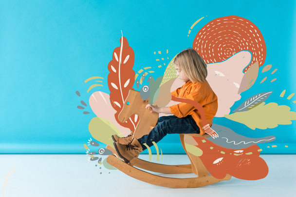 kid in jeans and orange shirt riding rocking horse on blue background with fairy nature illustration - Photo, Image