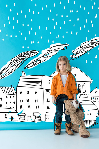 upset and adorable kid holding teddy bear on blue background with rain over buildings illustration - Photo, Image