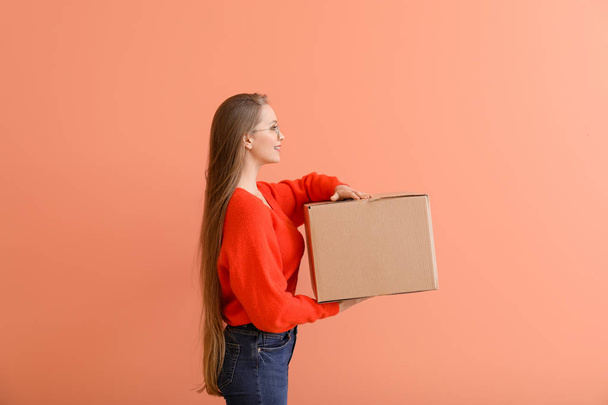 Young woman with cardboard box on color background - Zdjęcie, obraz