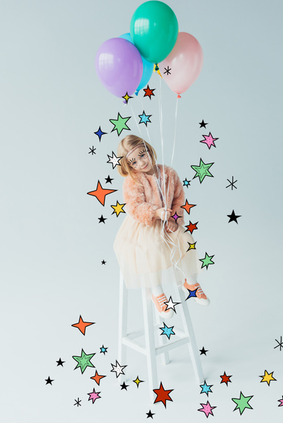 cute kid in faux fur coat and skirt sitting on highchair, looking at camera and holding balloons among stars - Foto, Imagem