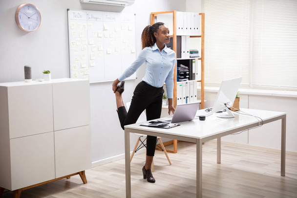 Young Businesswoman Doing Yoga Standing In Front Of Office Desk - Fotó, kép