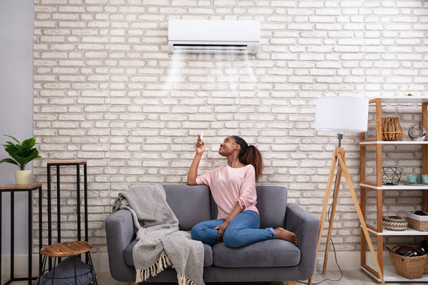 Young African Woman Switching On Air Conditioner With Remote Control At Home - Zdjęcie, obraz