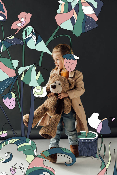 cute child in trench coat and jeans holding teddy bear on black background with fairy plants illustration - Фото, изображение
