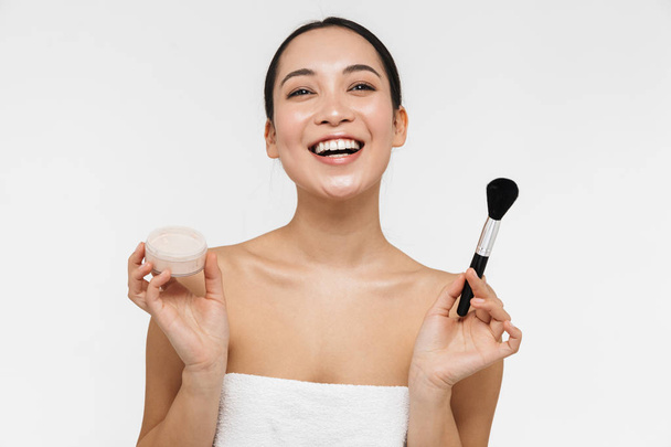 Pretty asian woman with healthy skin posing naked isolated over white wall background holding makeup brush. - Fotografie, Obrázek