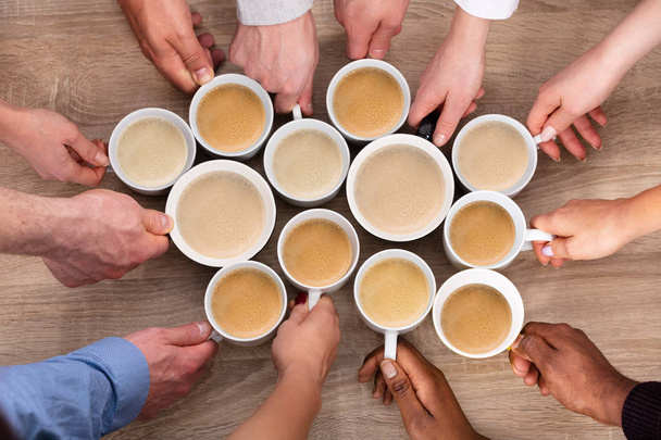 High Angle View Of People's Hand Holding Fresh Coffee Cups Against Wooden Background - Photo, image