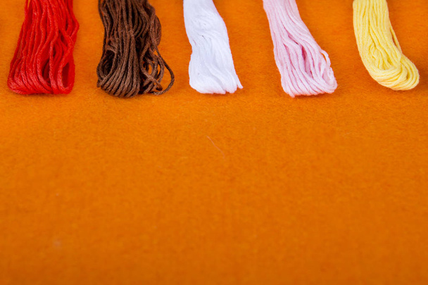 χρωματιστά νήματα σε πορτοκαλί φόντο. πολύχρωμα πολύχρωμα νήματα ουράνιο τόξο για κλείσιμο κέντημα, αξεσουάρ για ράψιμο και κέντημα στο Εργαστήρι ραπτικής - Φωτογραφία, εικόνα