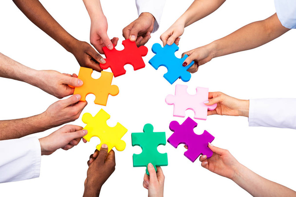 High Angle View Of Medical Team Solving Colorful Jigsaw Puzzle Against White Background - 写真・画像