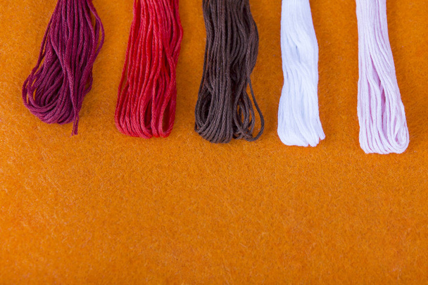 hilos de colores sobre un fondo naranja. hilos multicolores de arco iris multicolor para bordar de cerca, accesorios para coser y bordar en el taller de costura
 - Foto, Imagen