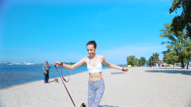 kaunis nuori hoikka urheilullinen nainen kävelee söpö tricolor Welsh Corgi koira hiekkarannalla aurinkoisena aamuna
. - Materiaali, video