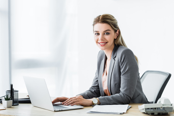 happy businesswoman sitting in office and working on laptop - Photo, Image