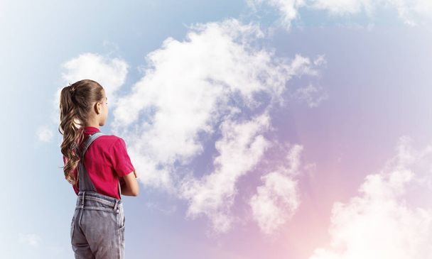 Little cute girl in overalls against sky background dreaming about future - Photo, image