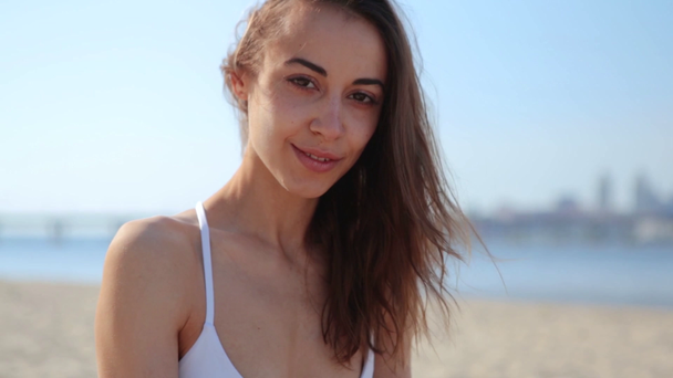 Gelukkig vrolijke gemengde race vrouw van Aziatische Kaukasische etniciteit zittend op het strand en kijken naar de camera, wind waait dames haar - Video