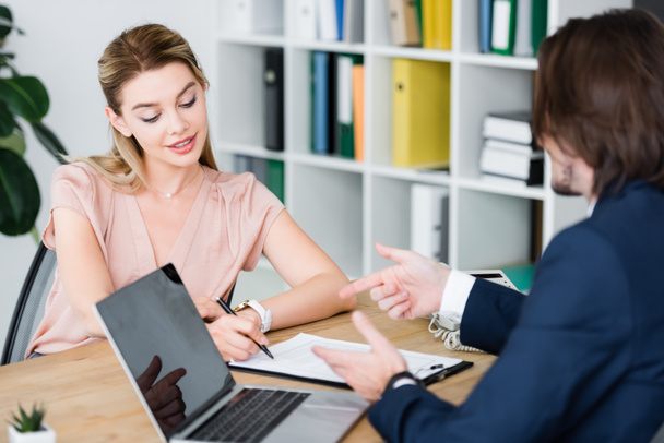 charming woman sitting in office with businessman and signing contract - Foto, Imagem