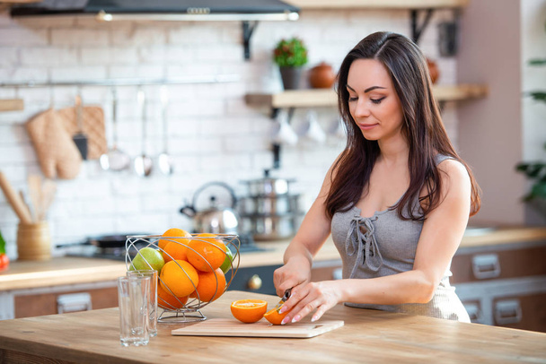 sporty young woman is cutting fresh orange for fruit juice in the kitchen. Horizontal indoors shot - Fotografie, Obrázek