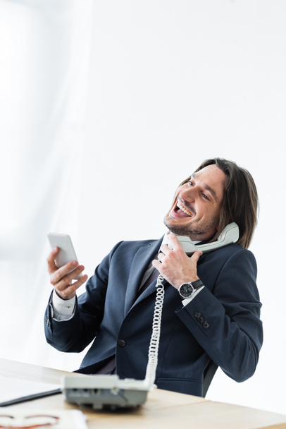 onnellinen komea liikemies puhuu puhelimessa, pitämällä älypuhelin ja kuulokkeet käsissä
 - Valokuva, kuva