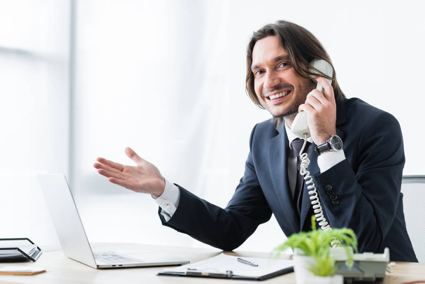 onnellinen liikemies puhuu puhelimessa toimistossa ja katselee kameraa
 - Valokuva, kuva