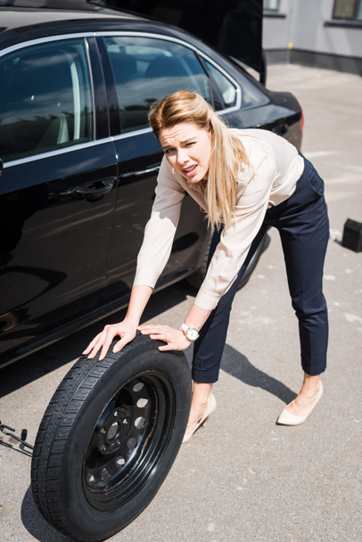 mujer de negocios mirando a la cámara, rodando nueva rueda y la fijación de automóviles rotos, concepto de seguro de coche
 - Foto, Imagen