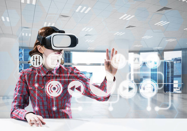 Horizontal shot of young and beautiful woman in checkered shirt using virtual reality headset and media interface while sitting inside bright office building. - 写真・画像