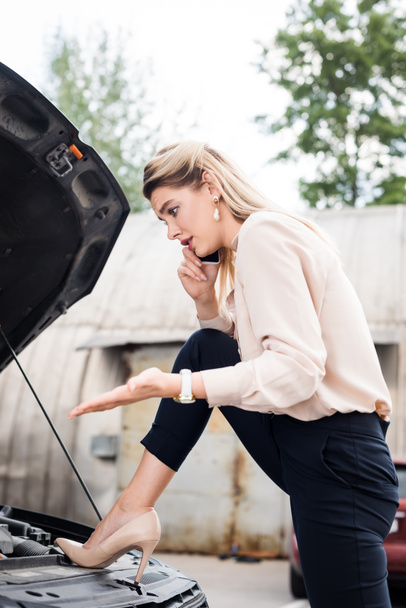 Geschäftsfrau spricht auf Smartphone und schaut kaputtes Auto an - Foto, Bild