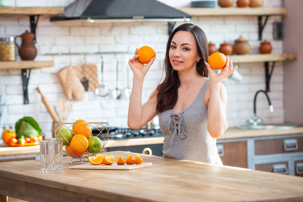 sporty young woman is cutting fresh orange for fruit juice in the kitchen. Horizontal indoors shot - Foto, Imagen
