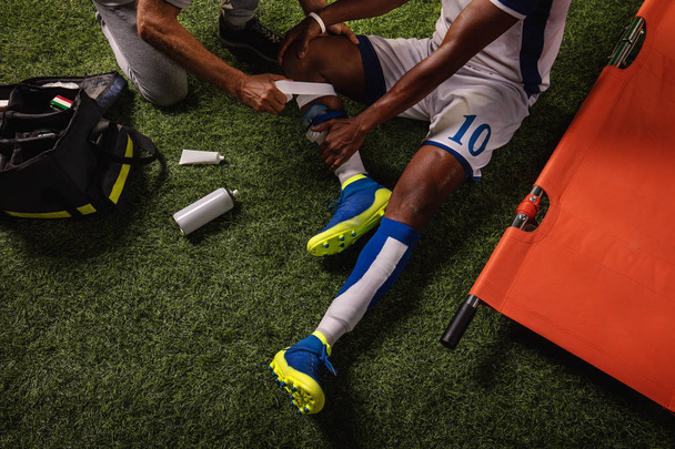 Ο ποδοσφαιριστής τραυματίστηκε στο γόνατο κατά τη διάρκεια του παιχνιδιού. Οι αθλητικοί γιατροί παρέχουν πρώτες βοήθειες στον παίκτη σε ένα επαγγελματικό γήπεδο ποδοσφαίρου. Κοντινό - Φωτογραφία, εικόνα