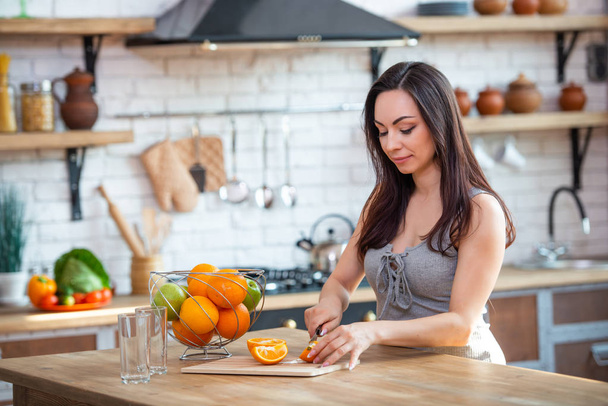 sporty young woman is cutting fresh orange for fruit juice in the kitchen. Horizontal indoors shot - Fotoğraf, Görsel