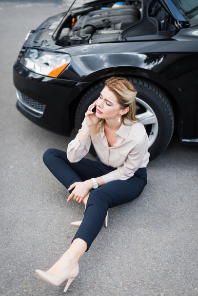 beautiful businesswoman talking on smartphone and sitting near broken auto, car insurance concept - Fotoğraf, Görsel