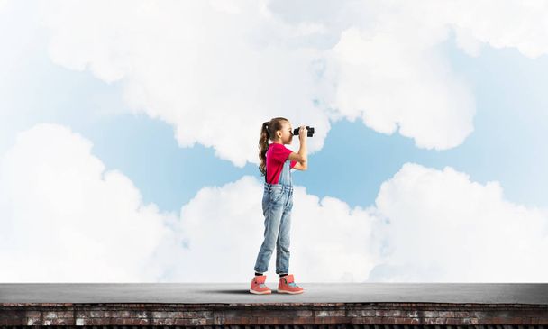 Cute girl of school age on building roof looking in binoculars - Photo, image