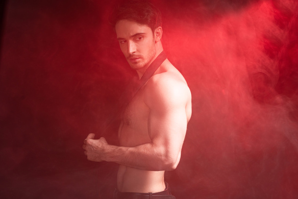 sin camisa sexy musculoso hombre mirando hacia otro lado en rojo humo
 - Foto, Imagen