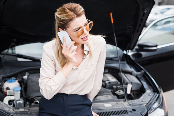 Geschäftsfrau schaut weg, telefoniert mit Smartphone und steht neben kaputtem Auto mit offenem Kofferraum, Kfz-Versicherungskonzept - Foto, Bild