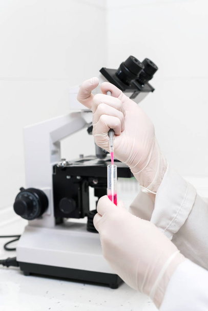 実験室のピペットの科学者の充填試験管。実験室の顕微鏡によるピペットを用いて試験管を充填する女性科学者のクローズアップビュー. - 写真・画像
