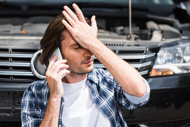 hombre hablando en el teléfono inteligente cerca de auto roto con capucha abierta, cogido de la mano en la cabeza, concepto de seguro de coche
 - Foto, Imagen