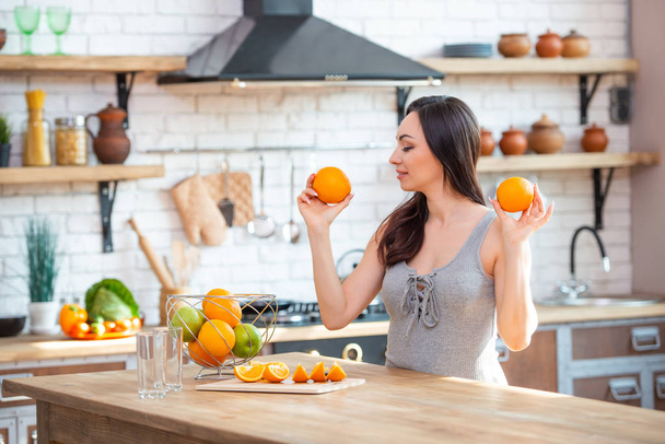 sporty young woman is cutting fresh orange for fruit juice in the kitchen. Horizontal indoors shot - Photo, image