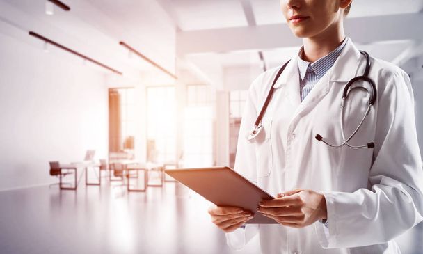 Close up of successful female doctor standing with tablet in hands indoors of white medical office building. Young woman doctor. Medical industry concept - Zdjęcie, obraz
