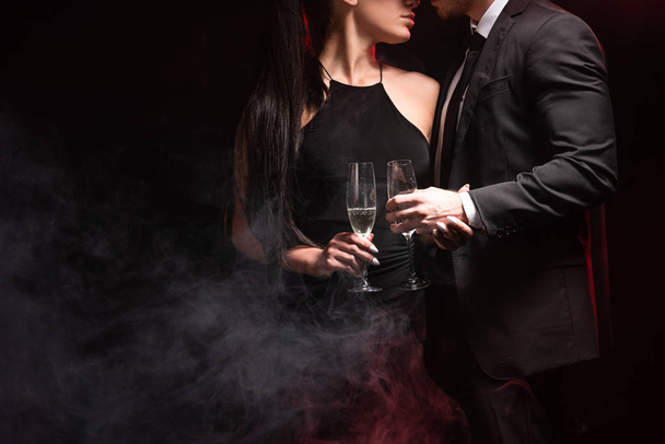 cropped view of stylish couple with glasses on champagne on black - Foto, Bild