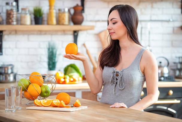 A young woman in a gray t-shirt holds an orange in her hand. Healthy eating concept. In the interior of the kitchen - Photo, image