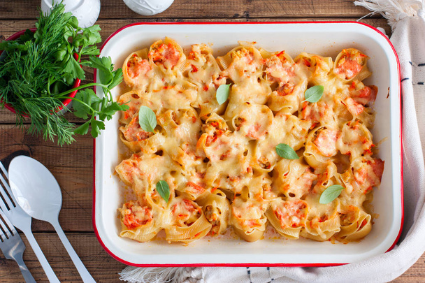 Baked large pasta stuffed with meat and cheese in enamel form on a wooden table, top view, horizontal - Foto, immagini