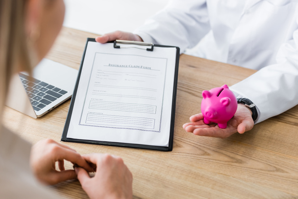 Ausgeschnittene Ansicht eines Arztes mit Antragsformular und Sparschwein in der Hand - Foto, Bild