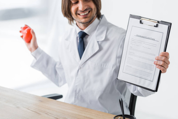 szczęśliwy lekarz posiadający czerwone serce i formularz roszczenia ubezpieczeniowego w rękach - Zdjęcie, obraz