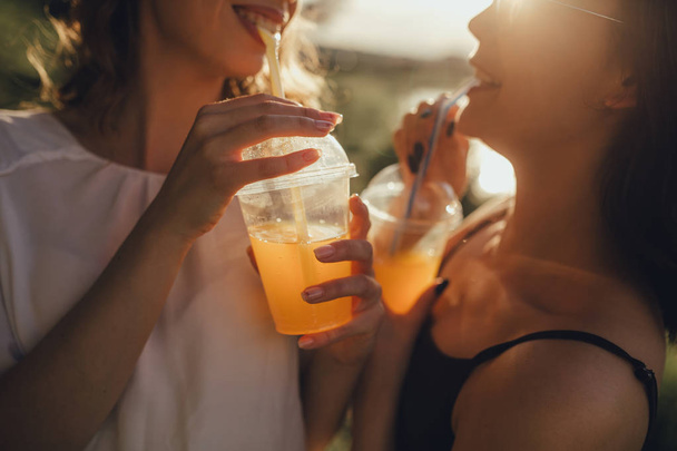 Coles fel. Két csinos lányok nővérek iszik lé szalma naplementekor, pozitív arckifejezés, kültéri - Fotó, kép